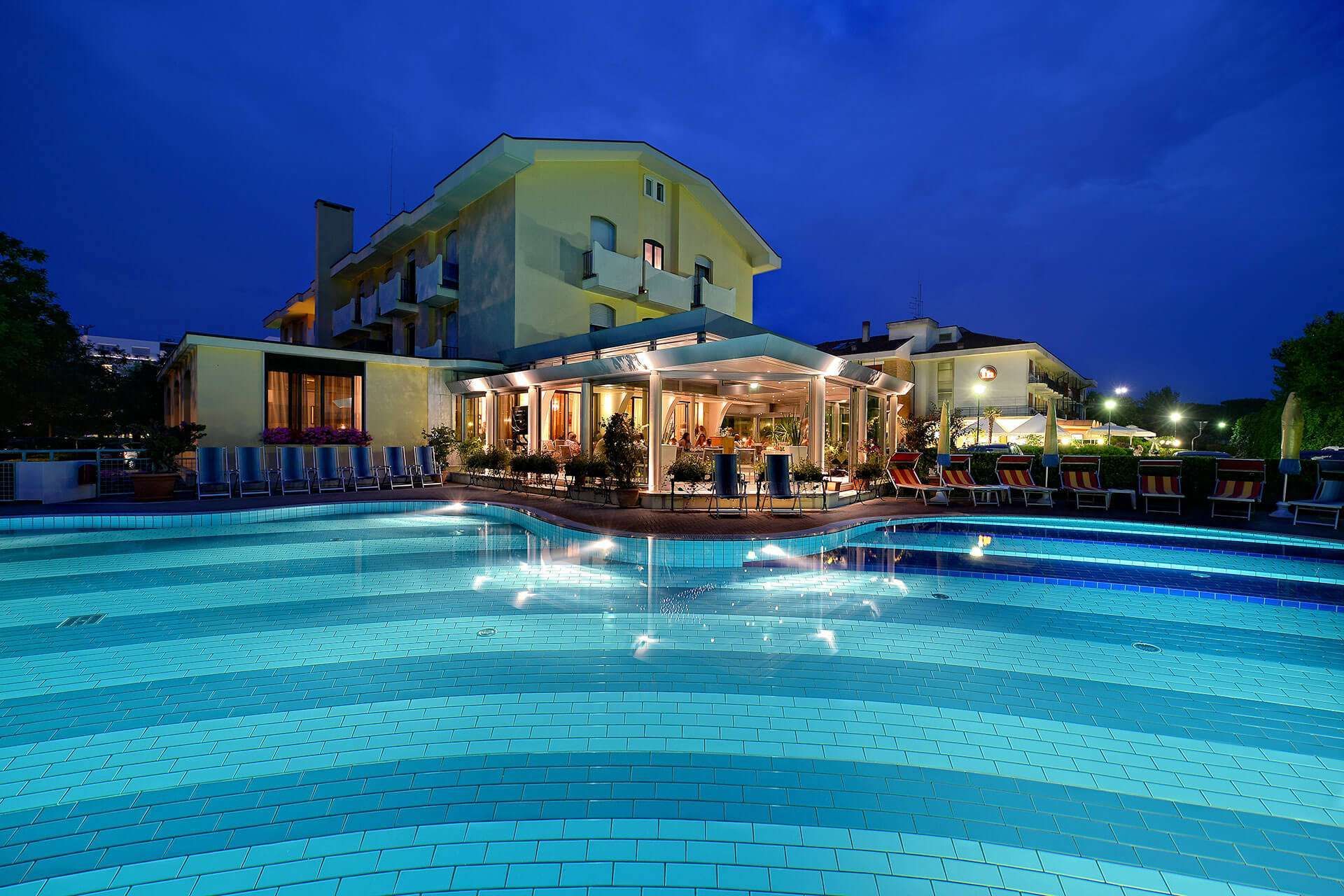 Piscina dell'hotel di notte con acqua illuminata e edificio sullo sfondo.