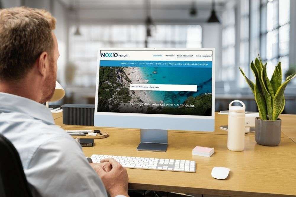 Uomo alla scrivania che usa il computer, è visibile la schermata di accesso al sito web. Beve un caffè.