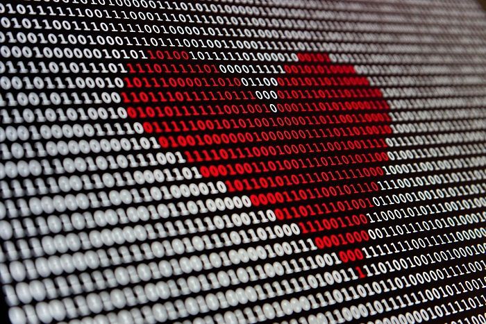 Cuore rosso formato da codice binario su sfondo nero, che simboleggia amore e tecnologia.