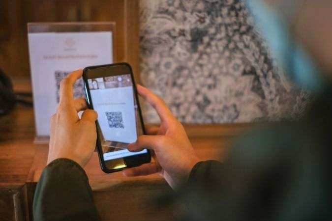 Persona che tiene in mano un telefono per scansionare un codice QR su un cartello in un ambiente scarsamente illuminato.