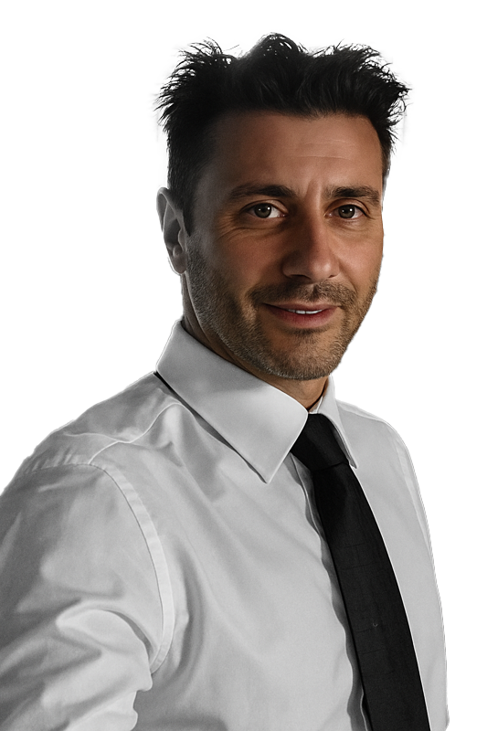 Un uomo in camicia bianca e cravatta nera sorride, guardando di lato, su uno sfondo bianco.