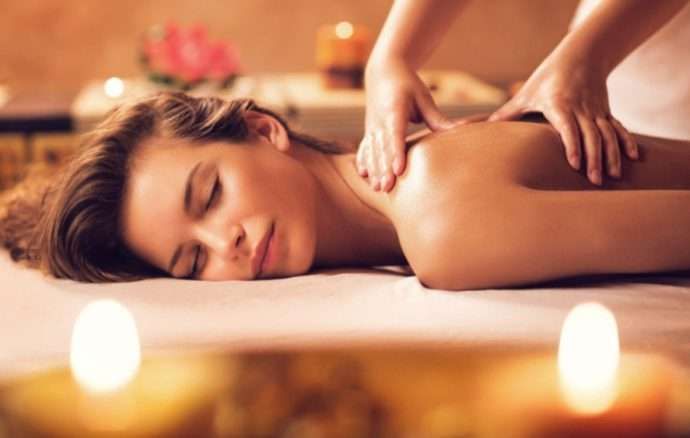 Donna che riceve un massaggio alla schiena in una spa, candele accese, occhi chiusi, in relax.