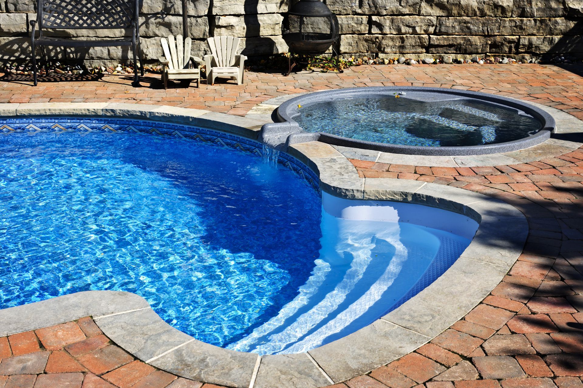 Backyard swimming pool with blue water and a circular hot tub beside a stone patio