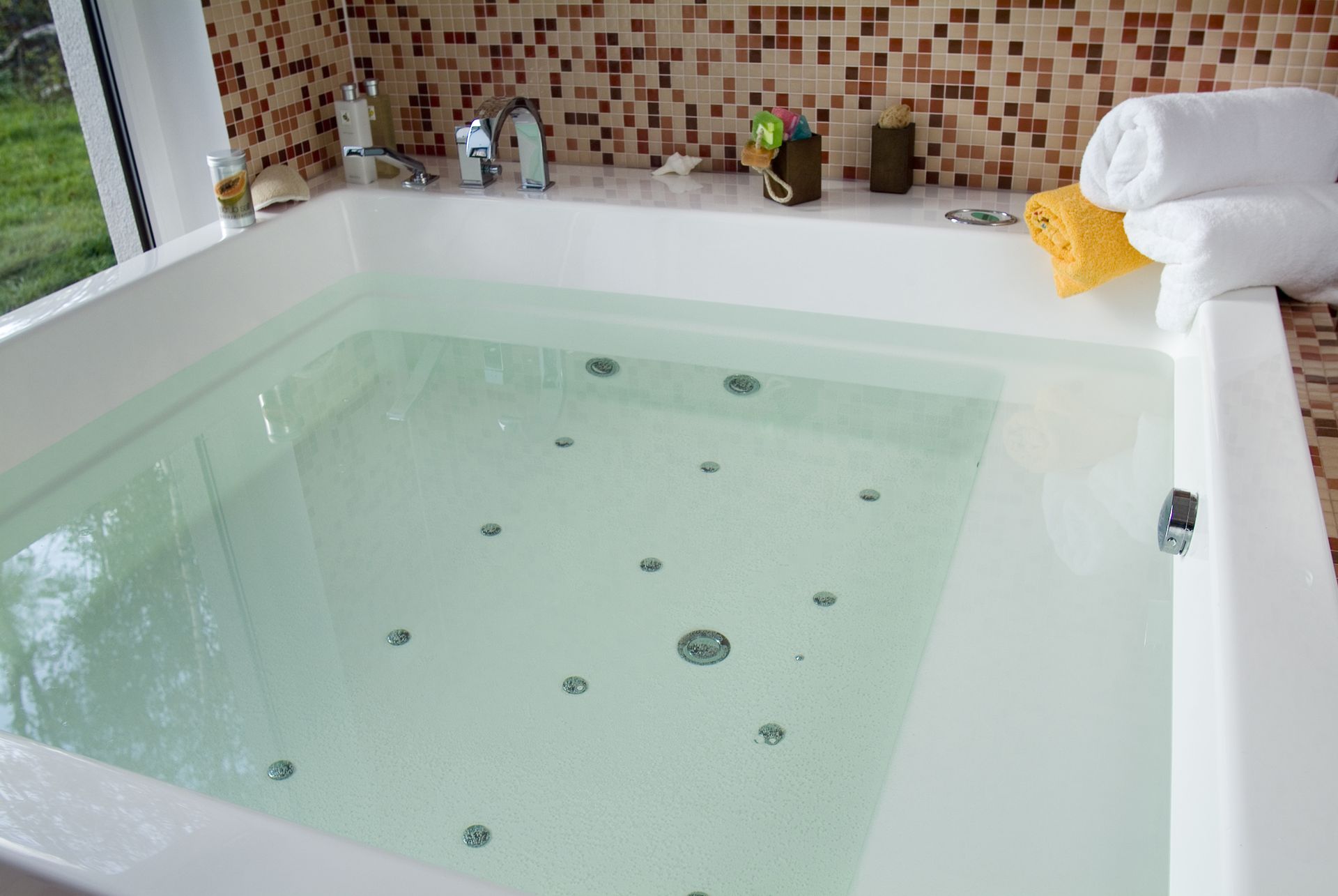 Large white indoor jacuzzi tub with clear water and mosaic tile backsplash