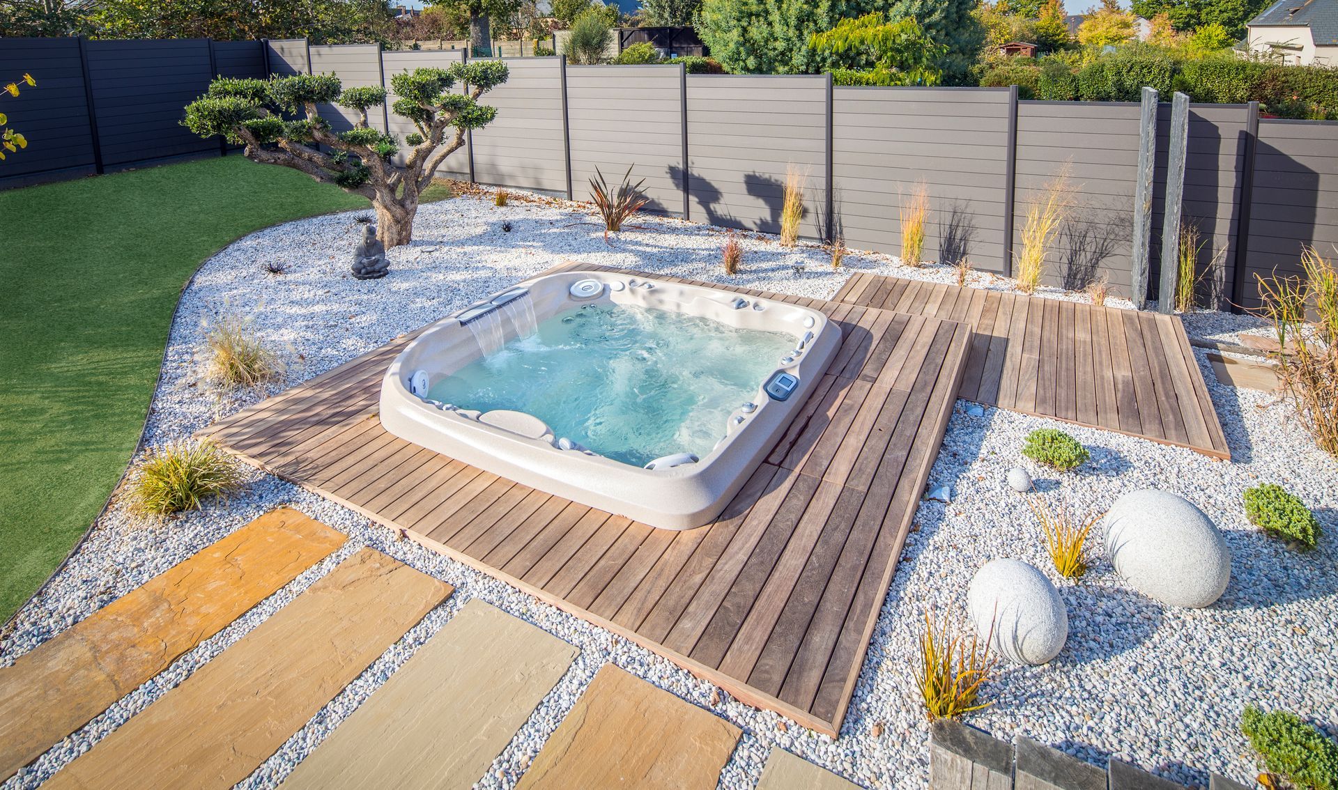 Small backyard spa pool with turquoise water on a wooden deck, surrounded by white gravel and landscaping.