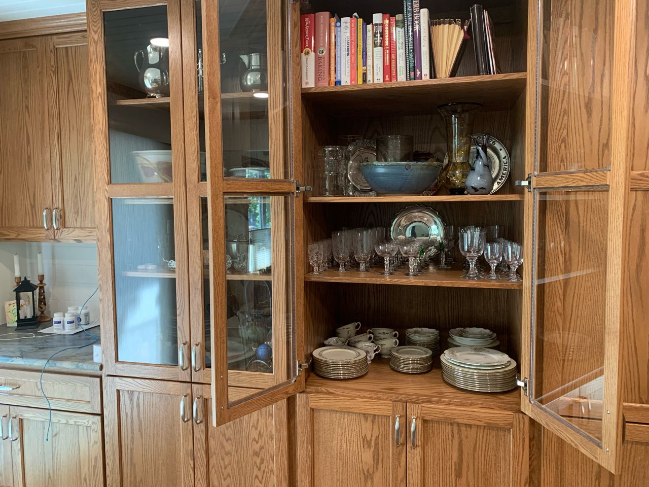 A wooden cabinet filled with plates , bowls , glasses , and books.