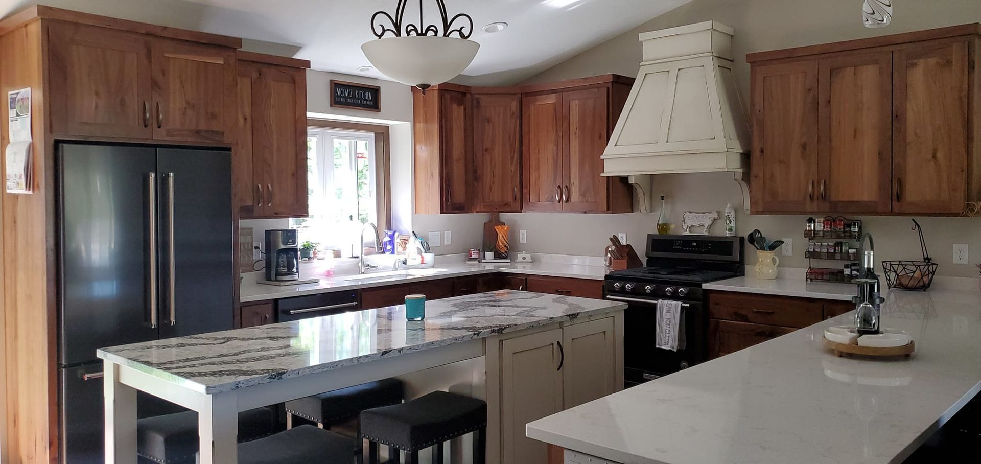 A kitchen with wooden cabinets , white counter tops , a refrigerator , a stove , and a large island.