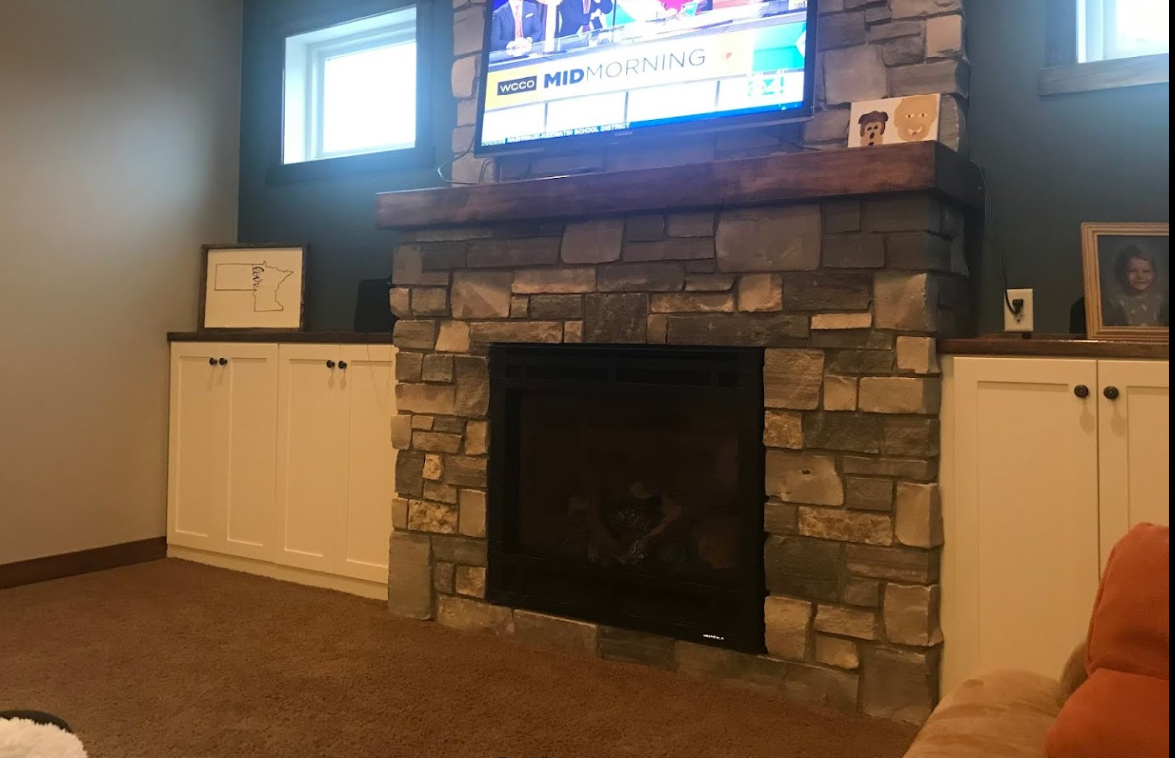 A living room with a stone fireplace and a flat screen tv.