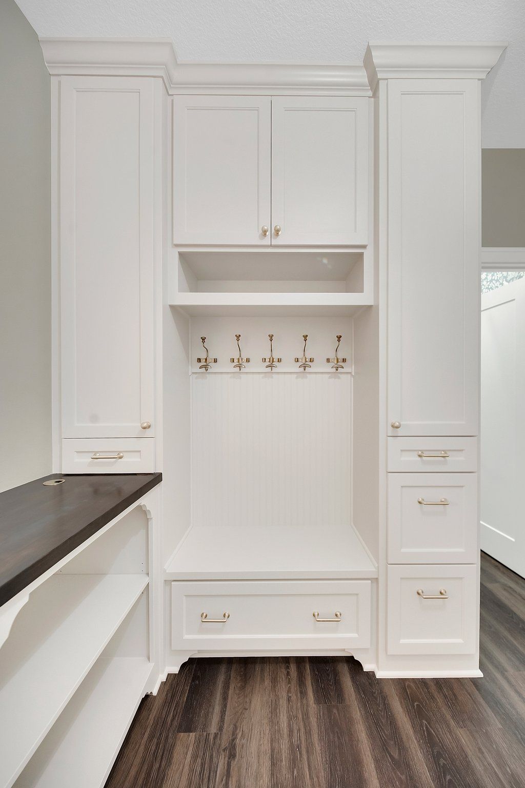 A mud room with white cabinets , drawers , and hooks.
