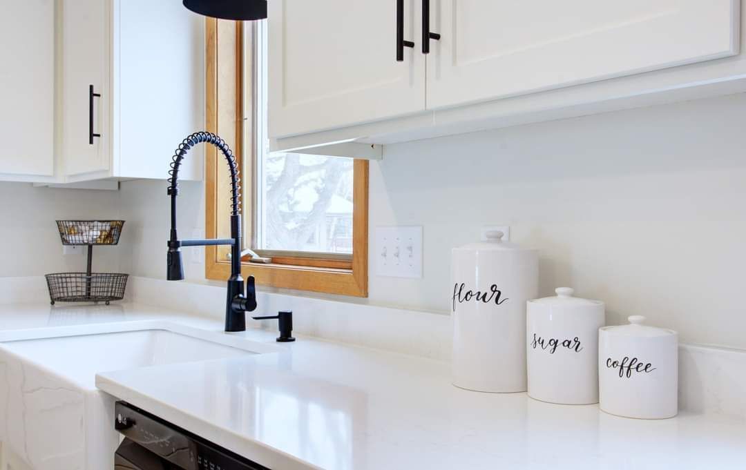 A kitchen with white cabinets , a sink , and a window.