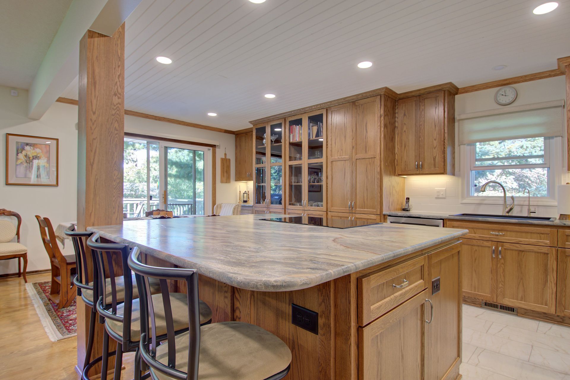 A kitchen with wooden cabinets , granite counter tops , stools and a large island.