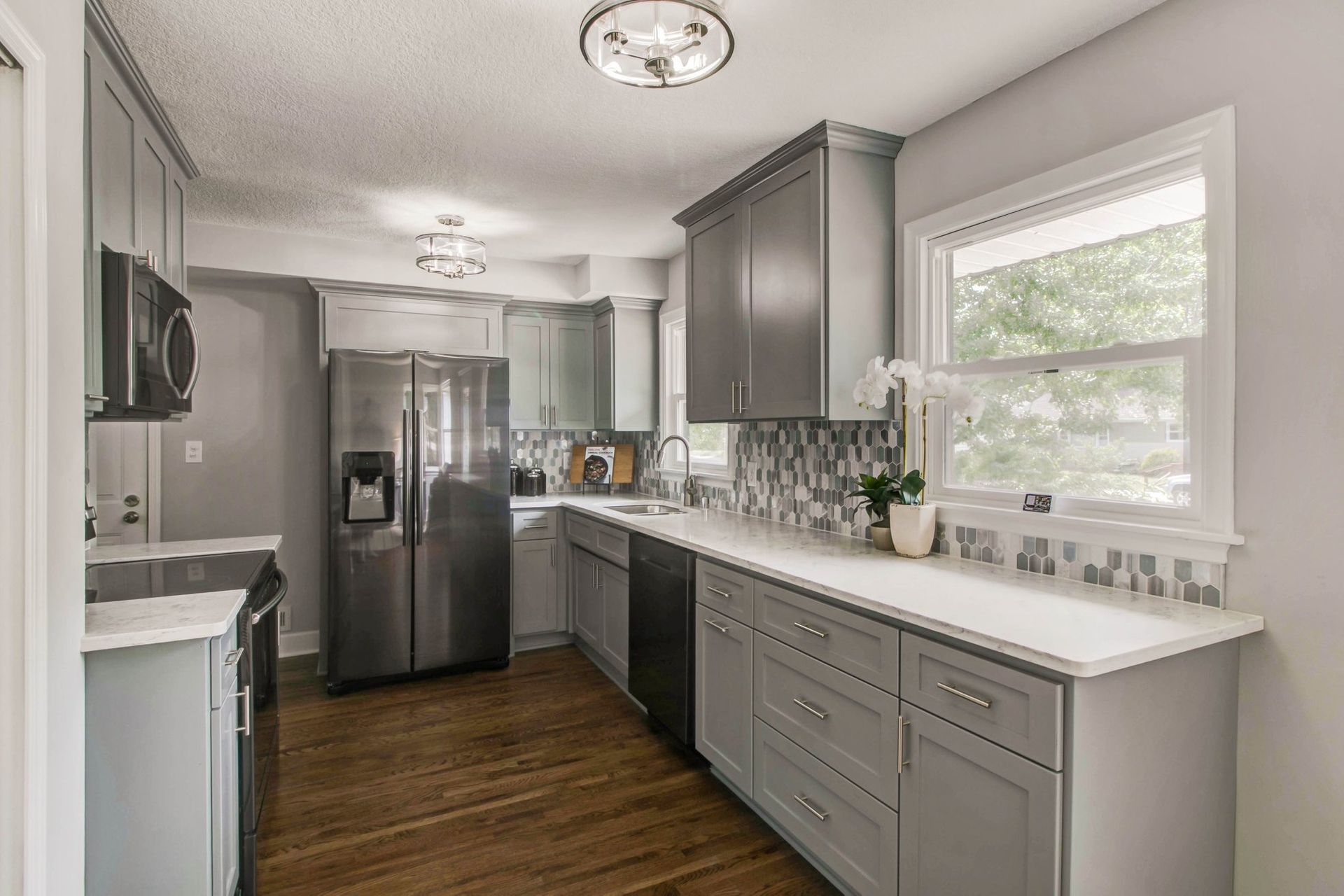 A kitchen with gray cabinets , stainless steel appliances , a refrigerator and a window.