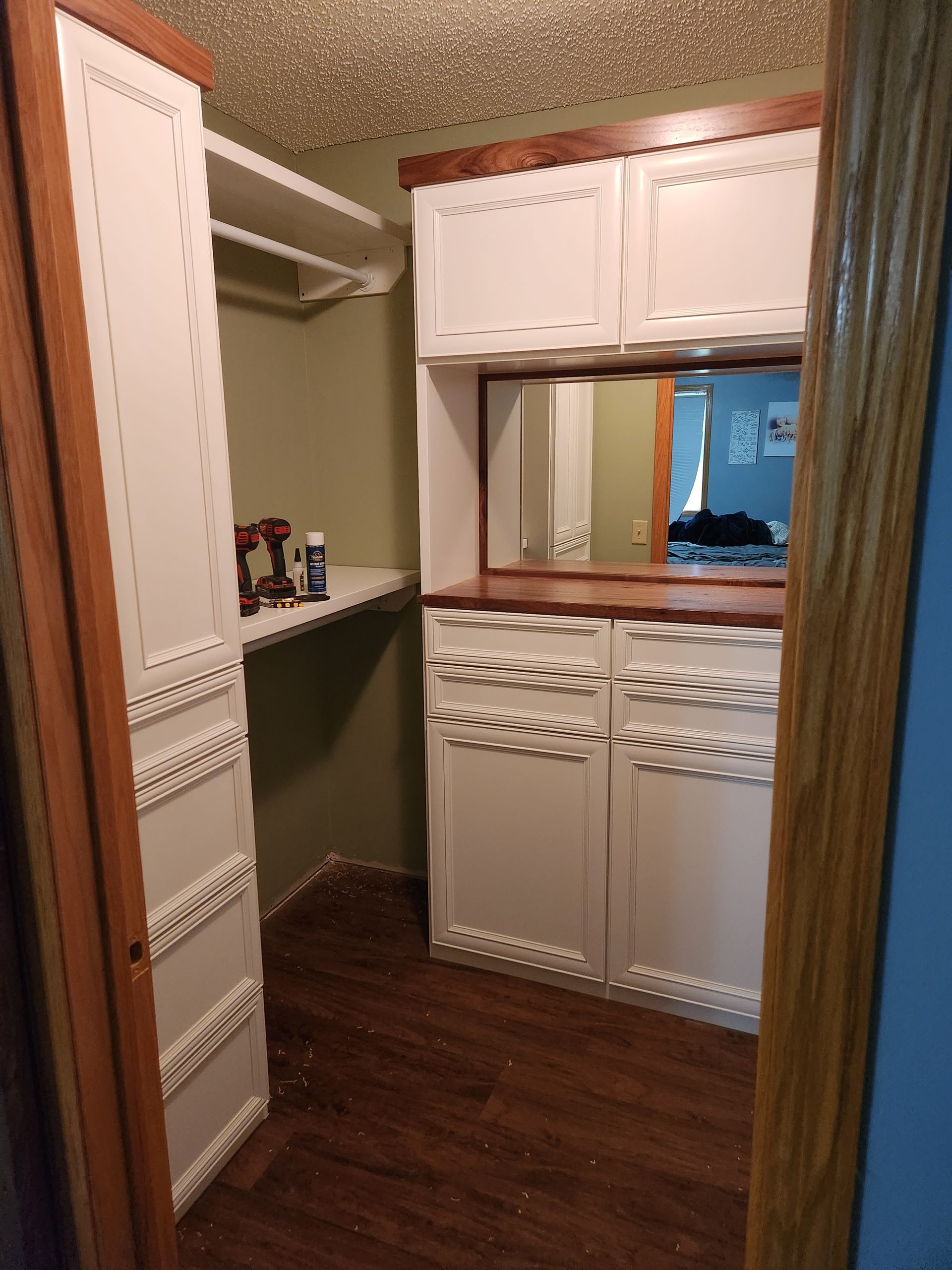 A walk in closet with white cabinets and a mirror