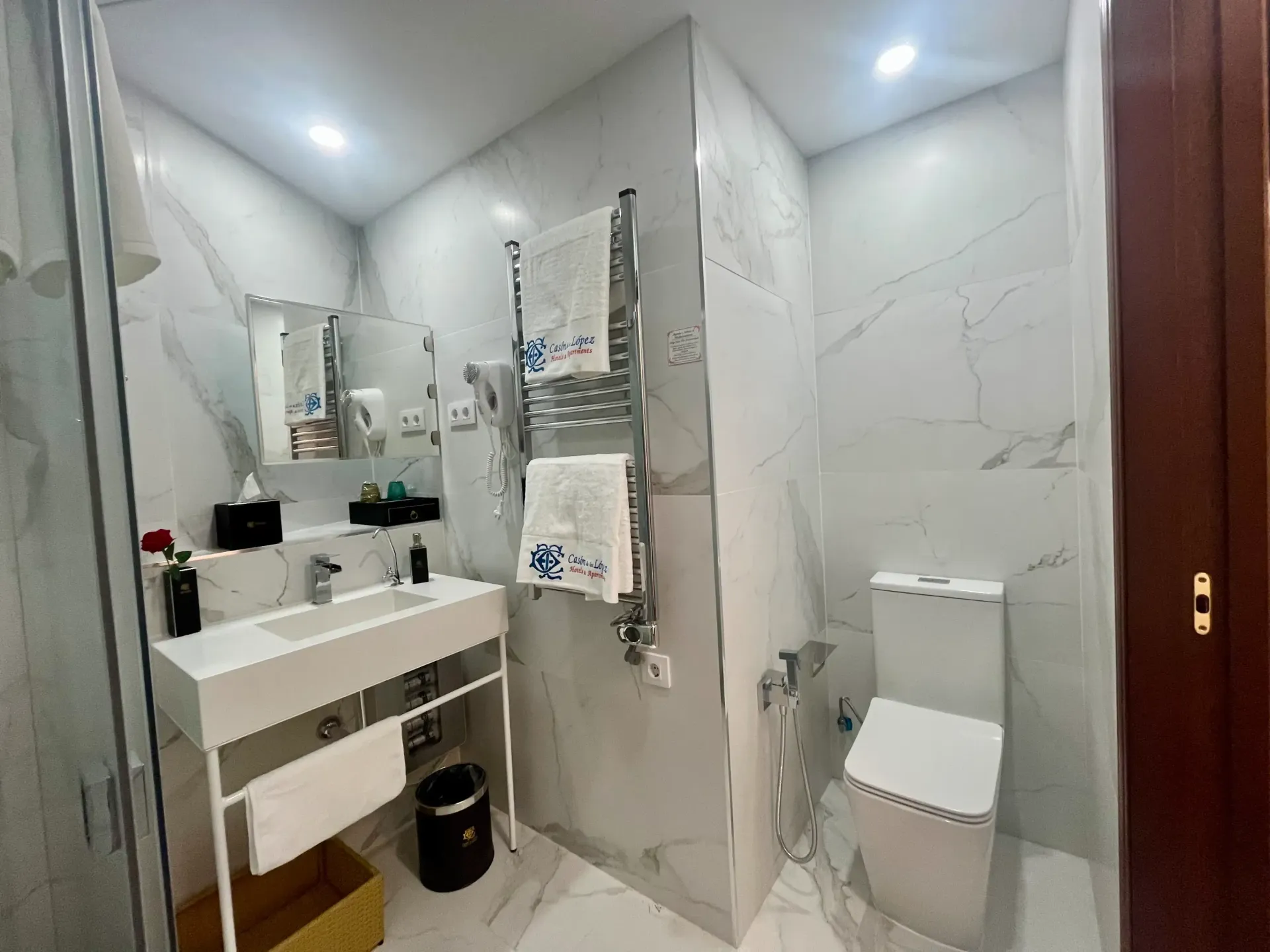 Baño moderno con azulejos blancos estilo mármol, lavabo suspendido, inodoro montado en la pared y toallero calefactable metálico.