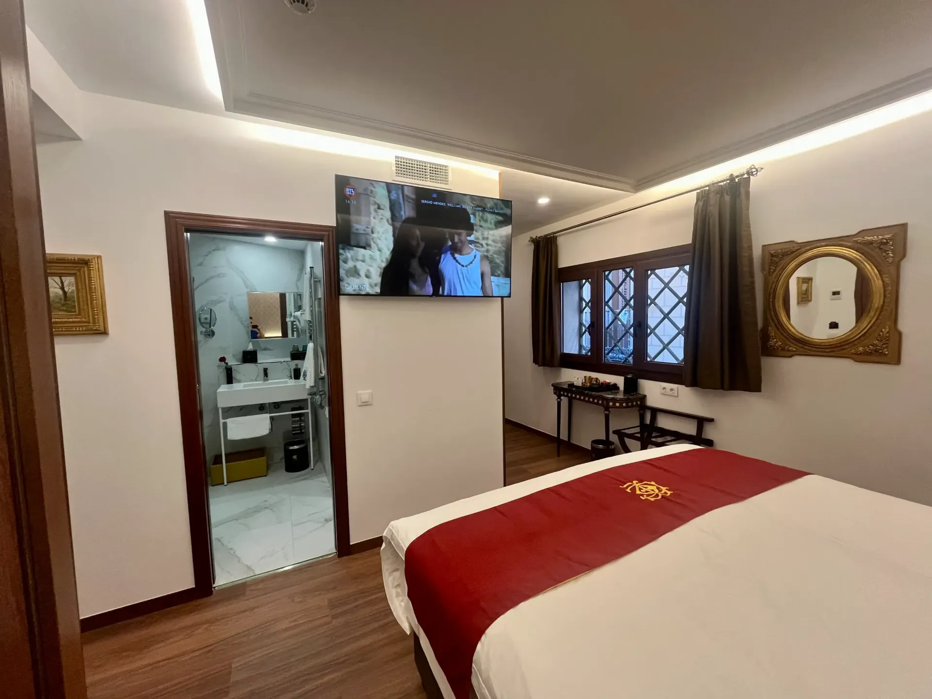 Una habitación de hotel con una cama con una estera roja, un televisor de pantalla plana en la pared y una puerta abierta que da al baño.