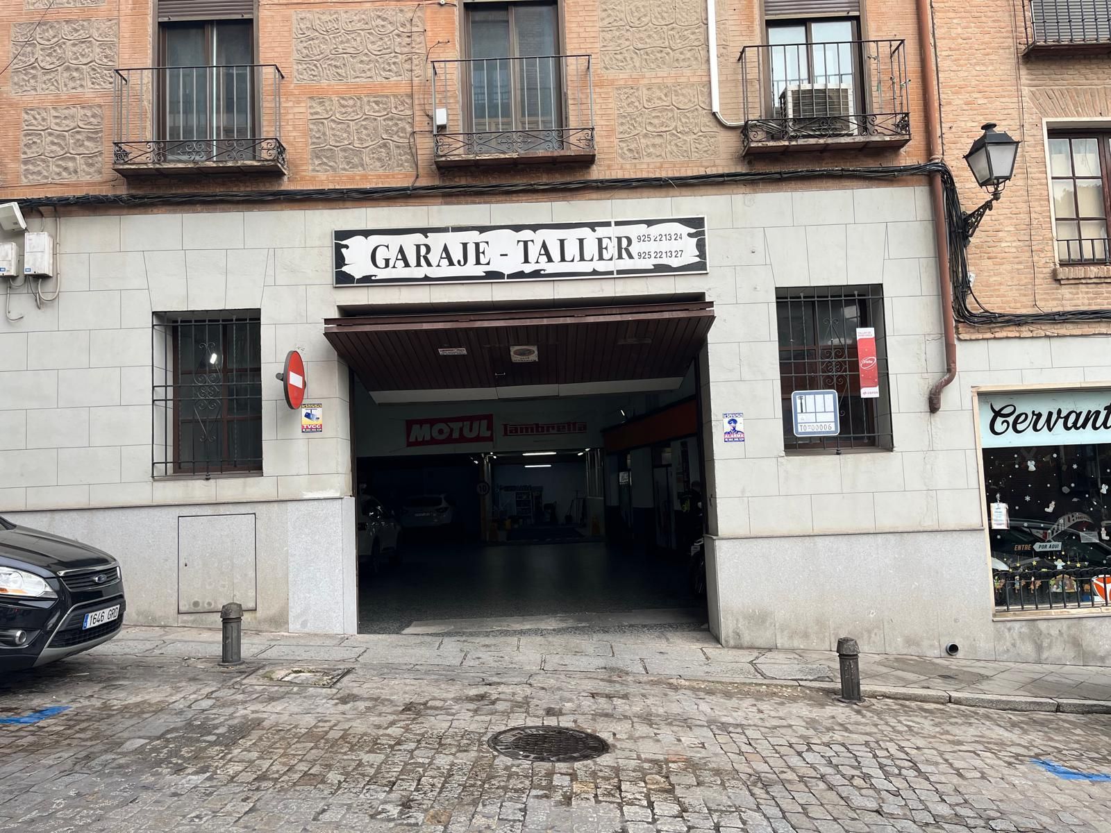 Vista a nivel de calle de la entrada de un garaje y taller de reparación de automóviles en una calle empedrada, en un edificio histórico de ladrillo.