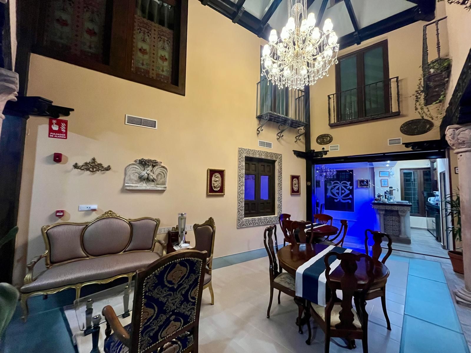 Un vestíbulo de hotel clásico, con techos altos, una gran lámpara de araña, un sofá y pequeñas mesas de comedor con sillas.