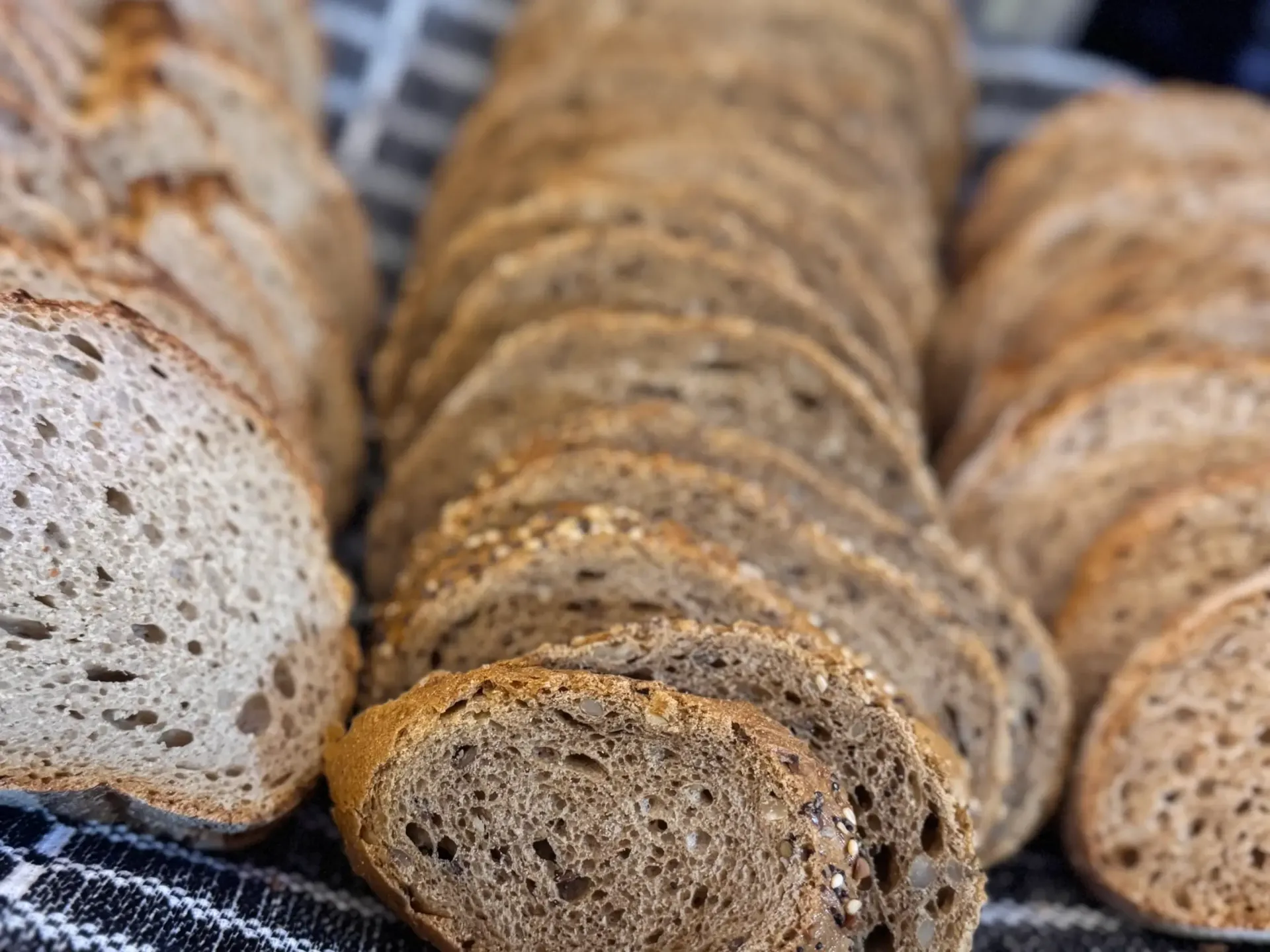 Primer plano de numerosas rebanadas de pan artesanal integral con semillas visibles, dispuestas en filas sobre un paño blanco y negro.