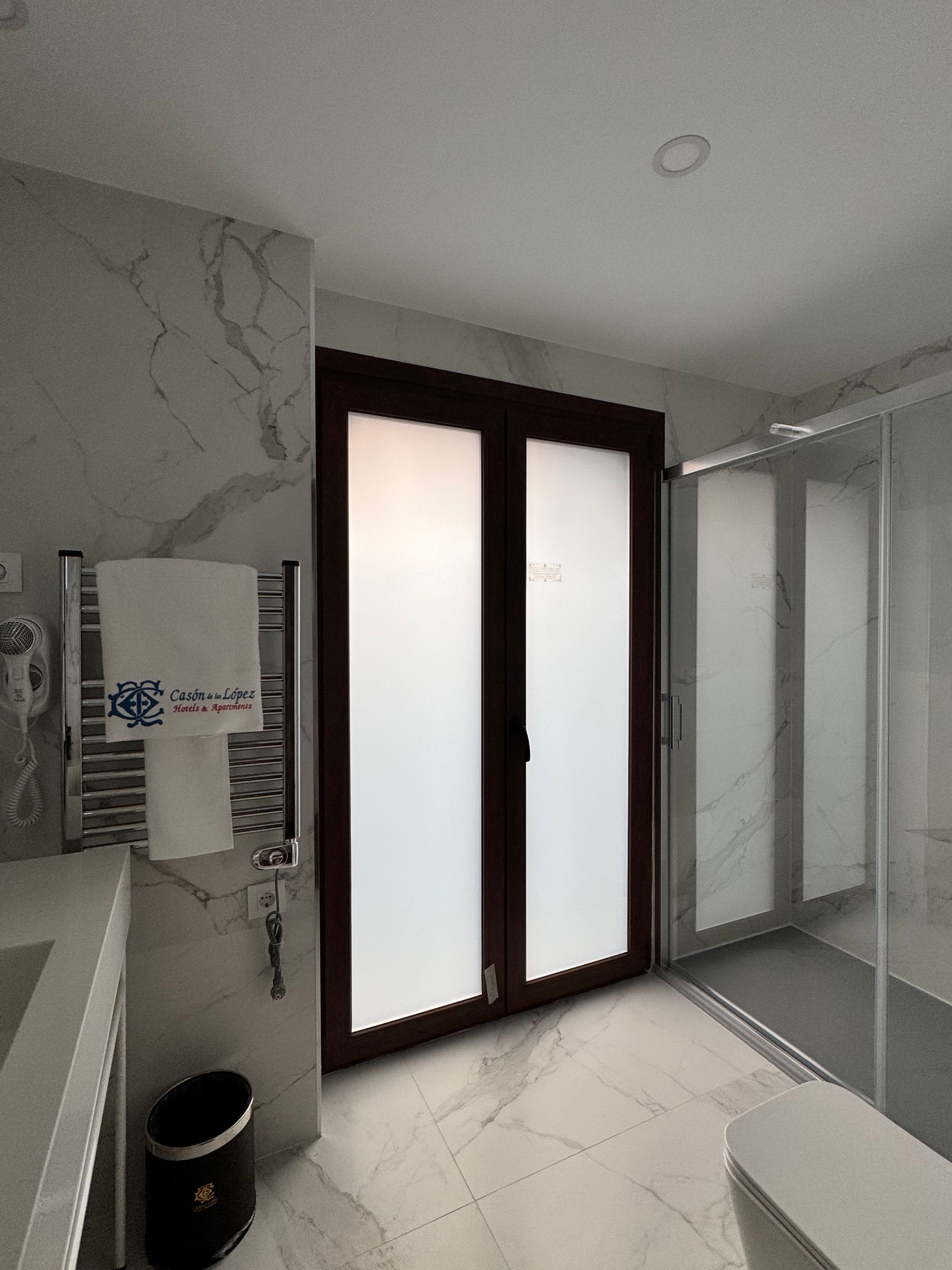 Un baño moderno con azulejos de mármol, cabina de ducha de cristal, toallero con toallas colgantes y puertas de cristal esmerilado.