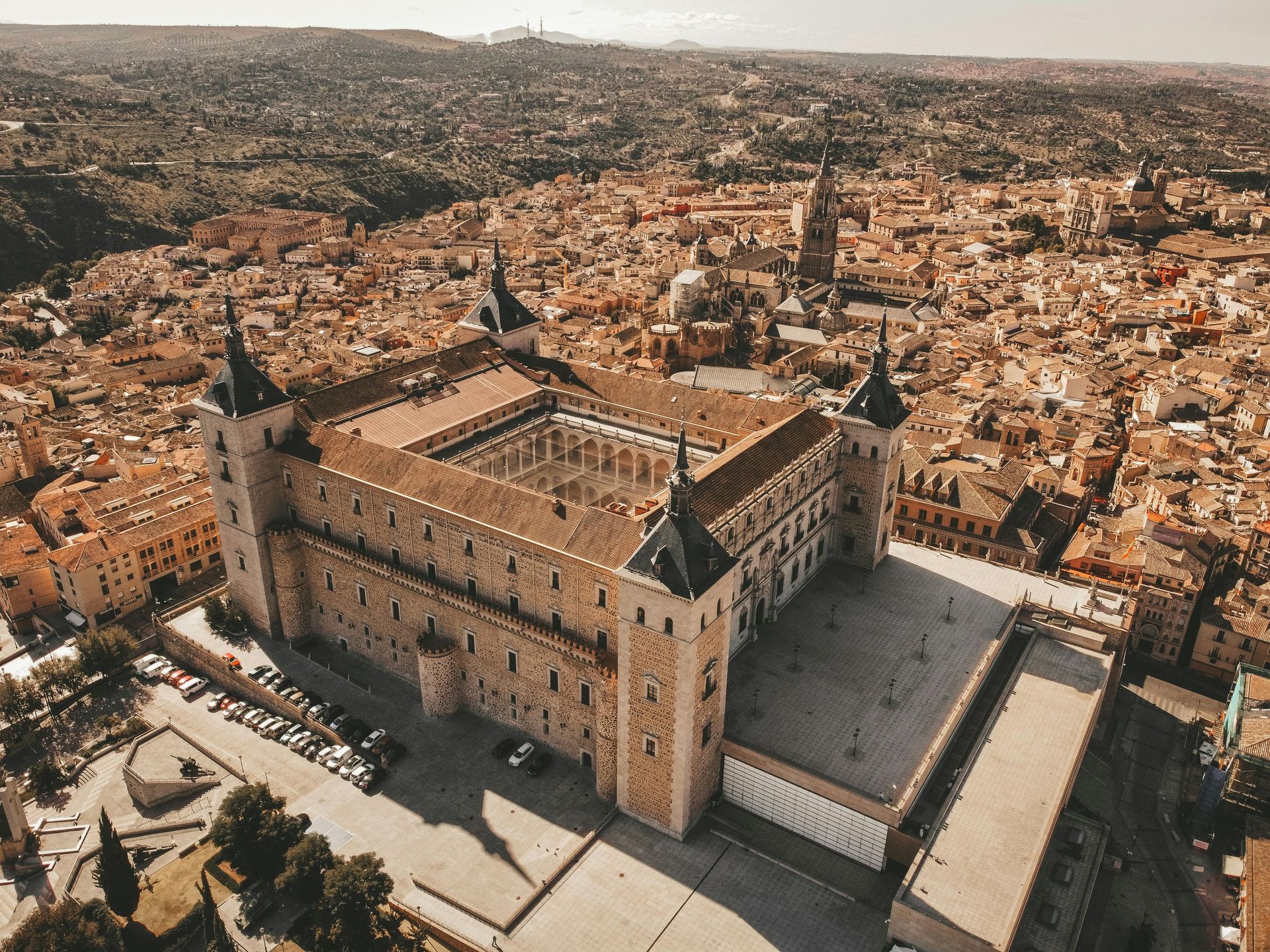 Vista aérea del Alcázar de Toledo, un gran palacio-fortaleza de piedra rodeado por una densa ciudad histórica de color tostado.