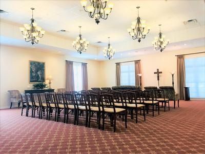Funeral home chapel with rows of chairs, chandeliers, and a cross.