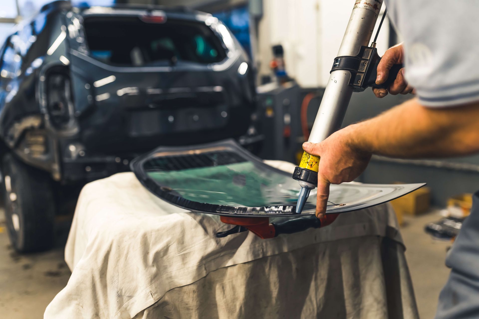 Auto body worker repairing a car windshield with a suction tool in a garage