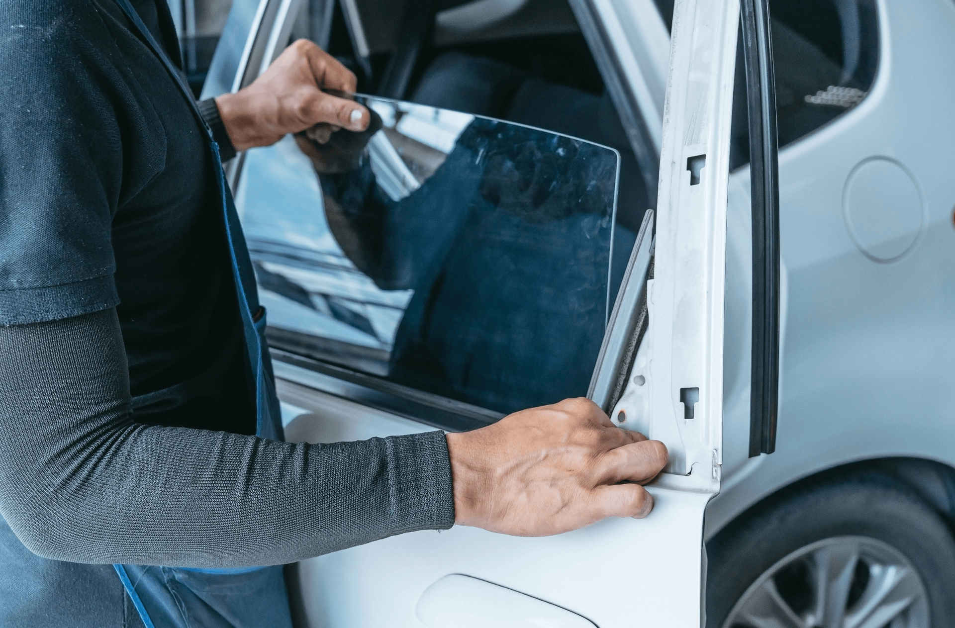 Person tinting a car window with dark film on a white vehicle