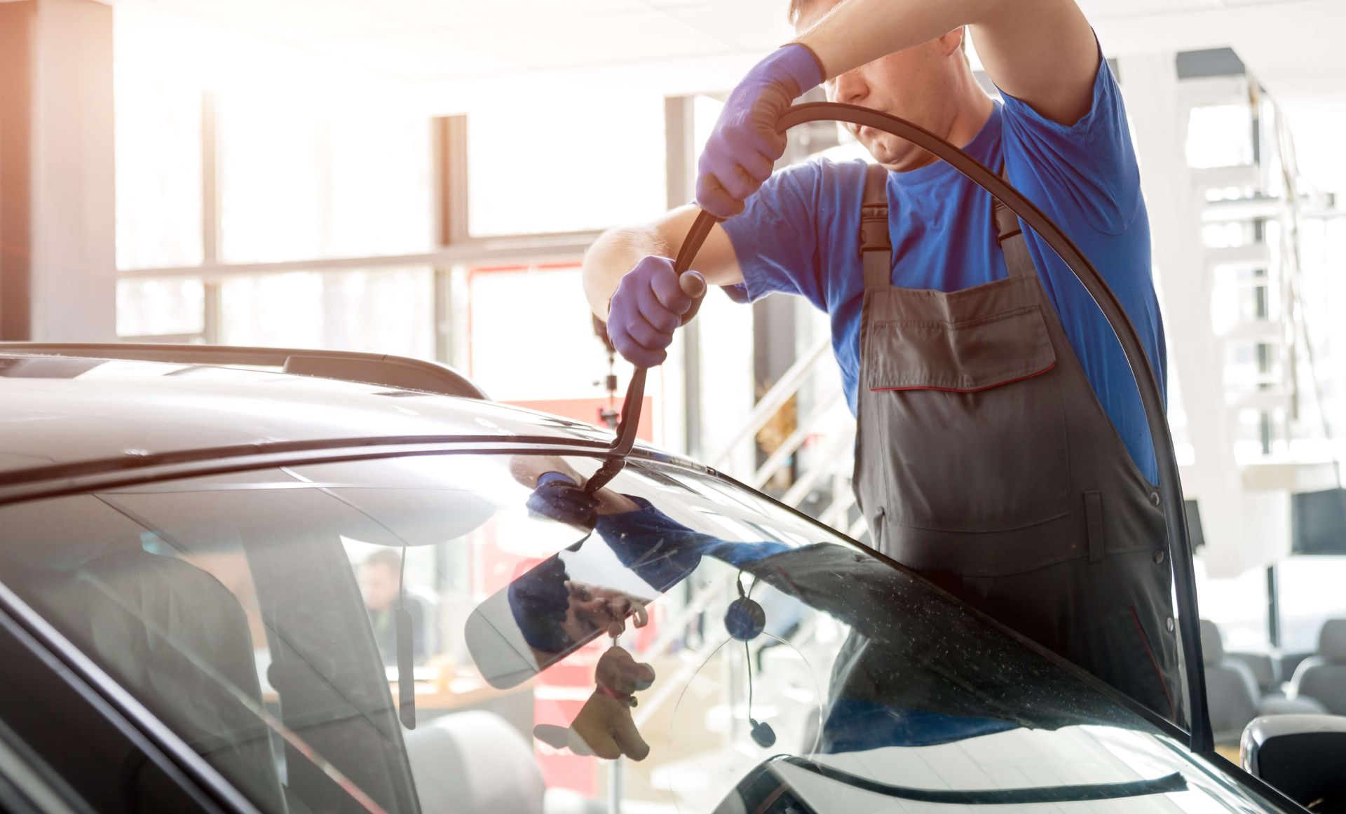 Person cleaning a car windshield in a bright garage, using a cloth and spray bottle