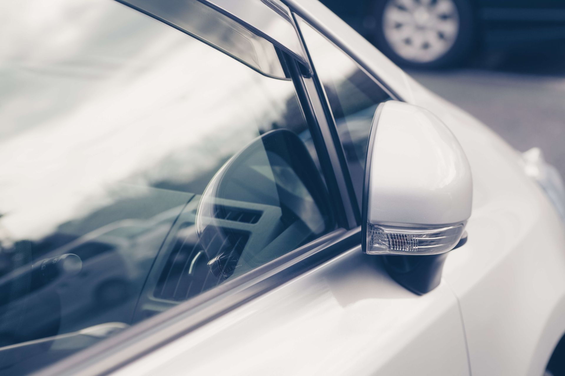 Close-up of a white car’s side mirror and window with blurred reflections.