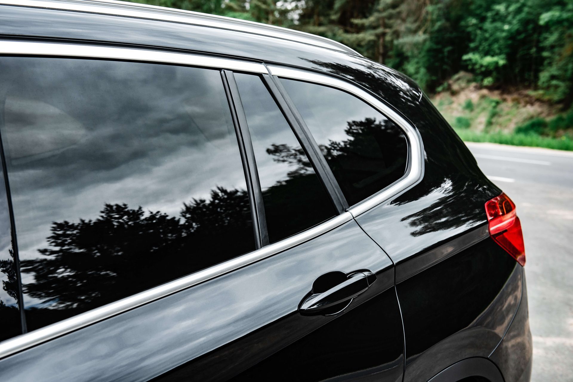 Black car side with tinted windows parked on a tree-lined road