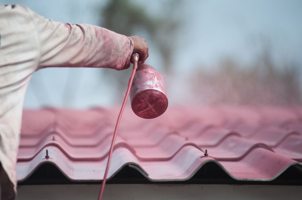 Person Spray Painting A Red Sealant Onto A Corrugated Roof — TMP Painting Services in Beaconsfield, QLD