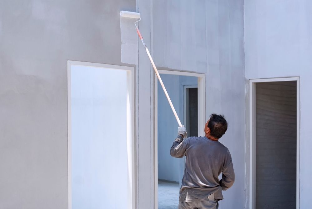 Person paints a light gray interior wall with a roller, using an extension pole — TMP Painting Services in Beaconsfield, QLD
