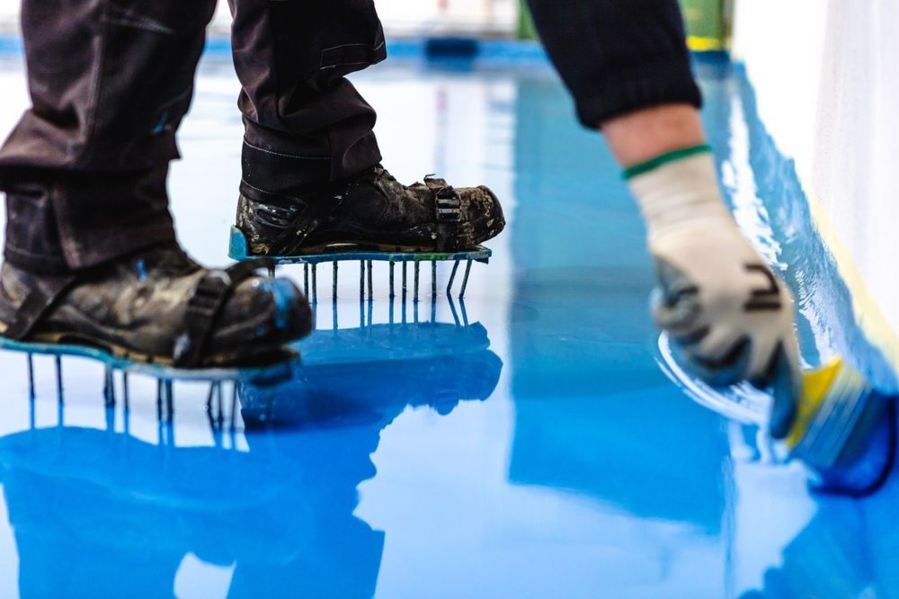 Person Applying Blue Epoxy Flooring With Spiked Shoes — TMP Painting Services in Beaconsfield, QLD