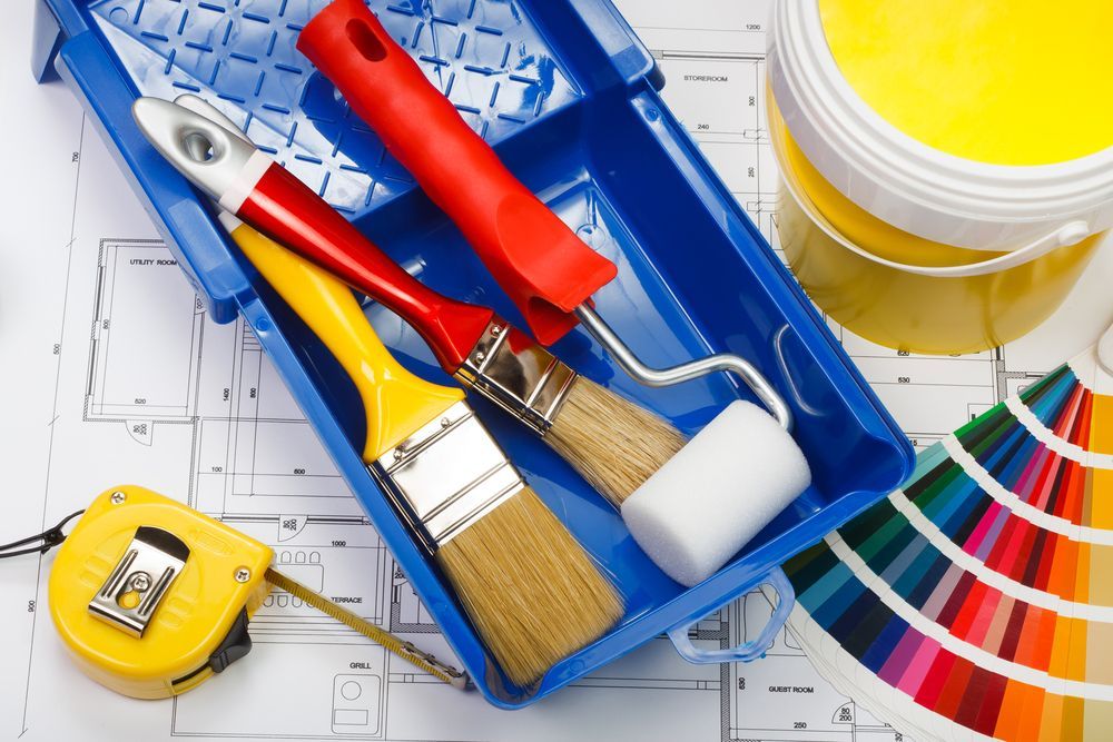 Paint supplies: paint tray, brushes, roller, yellow paint can, color swatches, measuring tape, on blueprint — TMP Painting Services in Paget, QLD