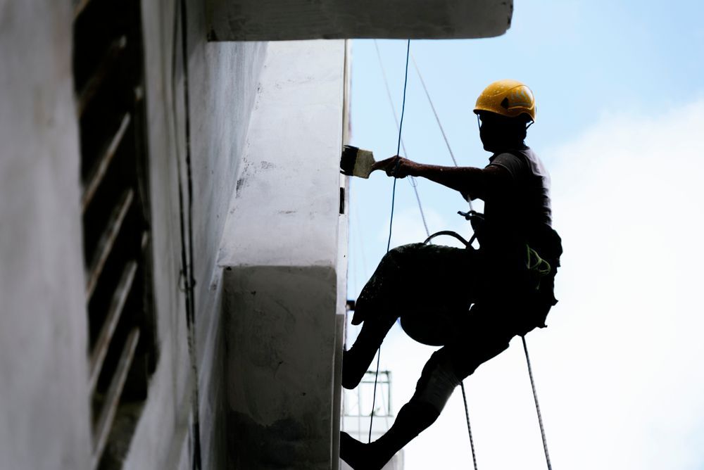 Construction worker paints a building facade while suspended by ropes — TMP Painting Services in Beaconsfield, QLD