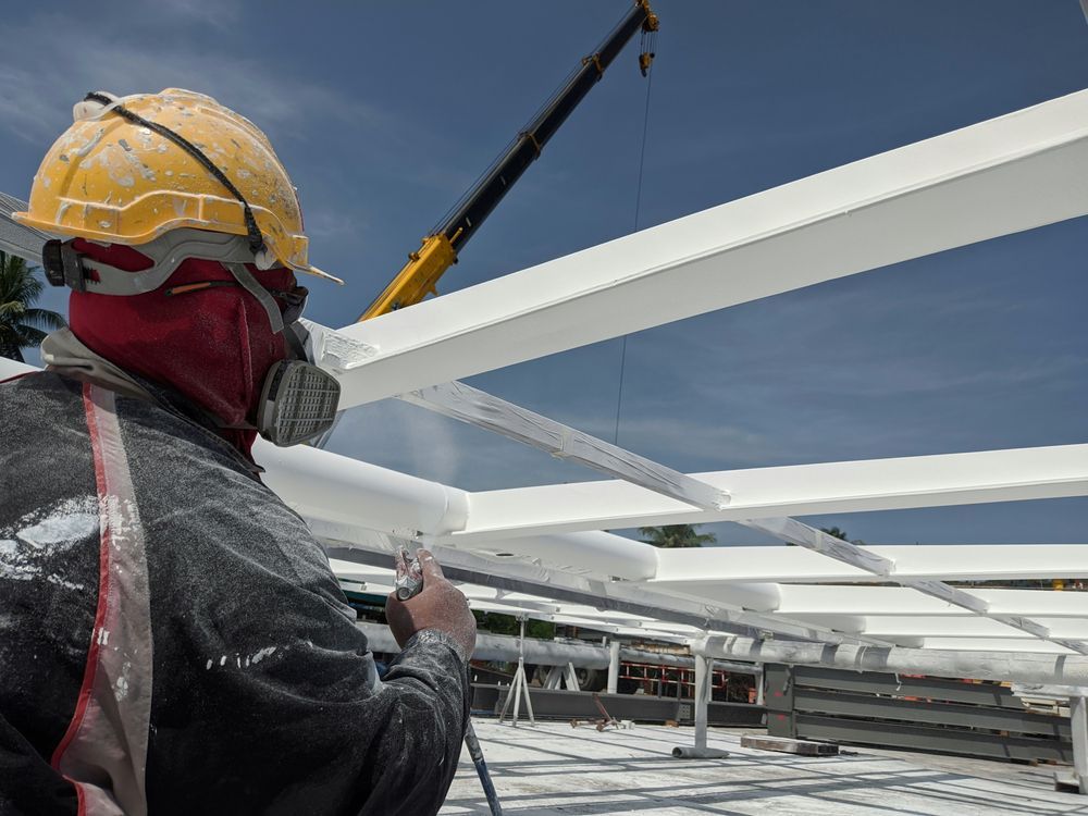Construction worker in respirator paints white beams with spray gun under a crane — TMP Painting Services in Beaconsfield, QLD