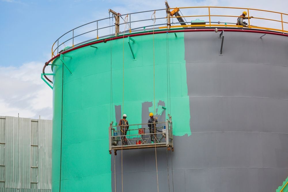 Two workers on a platform painting a large industrial tank, green paint on one side, gray on the other — TMP Painting Services in Beaconsfield, QLD