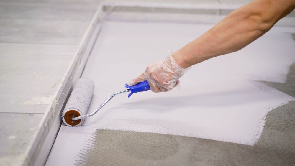 Person wearing gloves painting white paint on a gray surface with a roller — TMP Painting Services in Beaconsfield, QLD