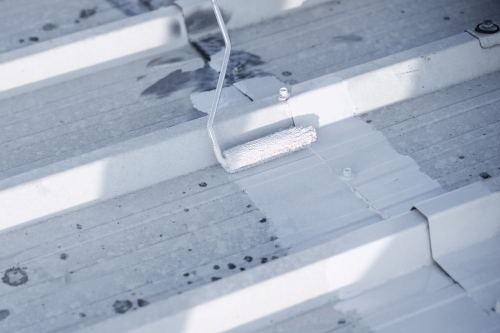 A person using a paint roller applies white paint to a corrugated metal roof — TMP Painting Services in Beaconsfield, QLD