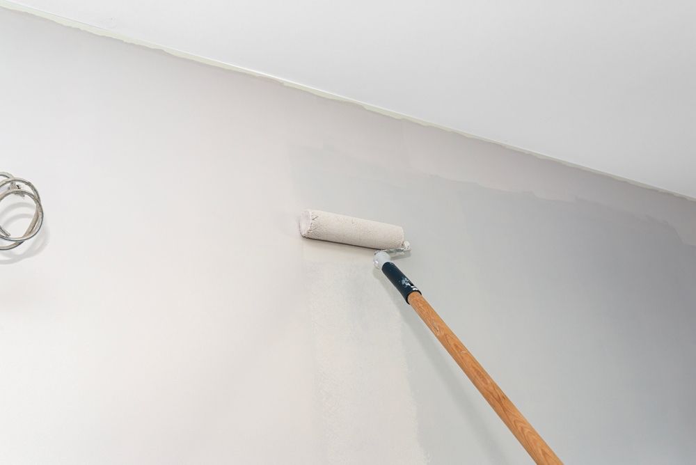White paint roller on a long wooden handle painting a white wall near a ceiling — TMP Painting Services in Beaconsfield, QLD