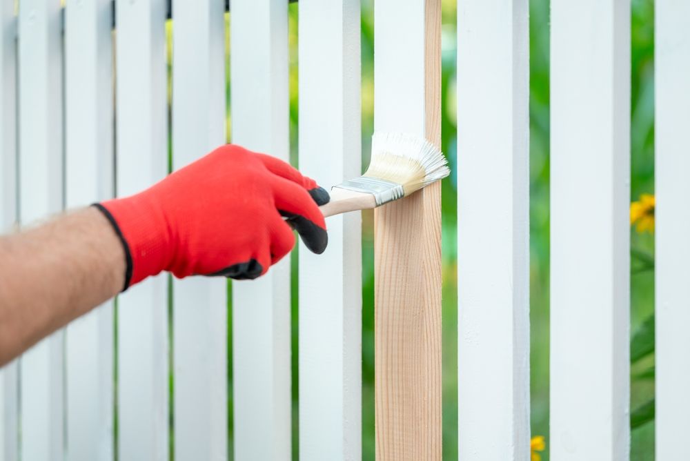 Person in red glove painting white fence with a brush — TMP Painting Services in Beaconsfield, QLD