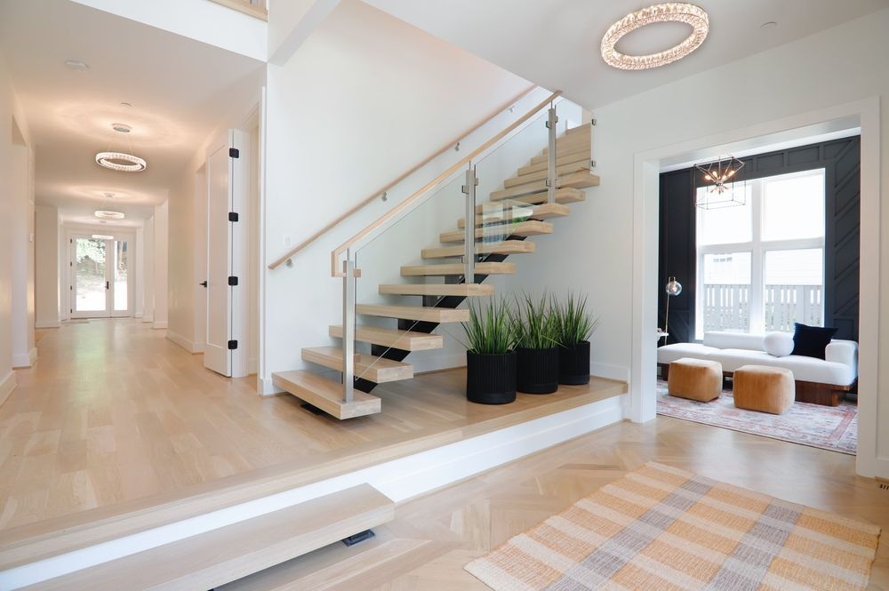 Bright, modern entryway with a floating staircase, white walls, and wood floors. A living area with black wall is visible — TMP Painting Services in Beaconsfield, QLD
