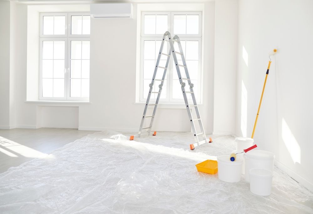 Bright room being painted with ladder, paint cans, roller and drop cloths — TMP Painting Services in Beaconsfield, QLD