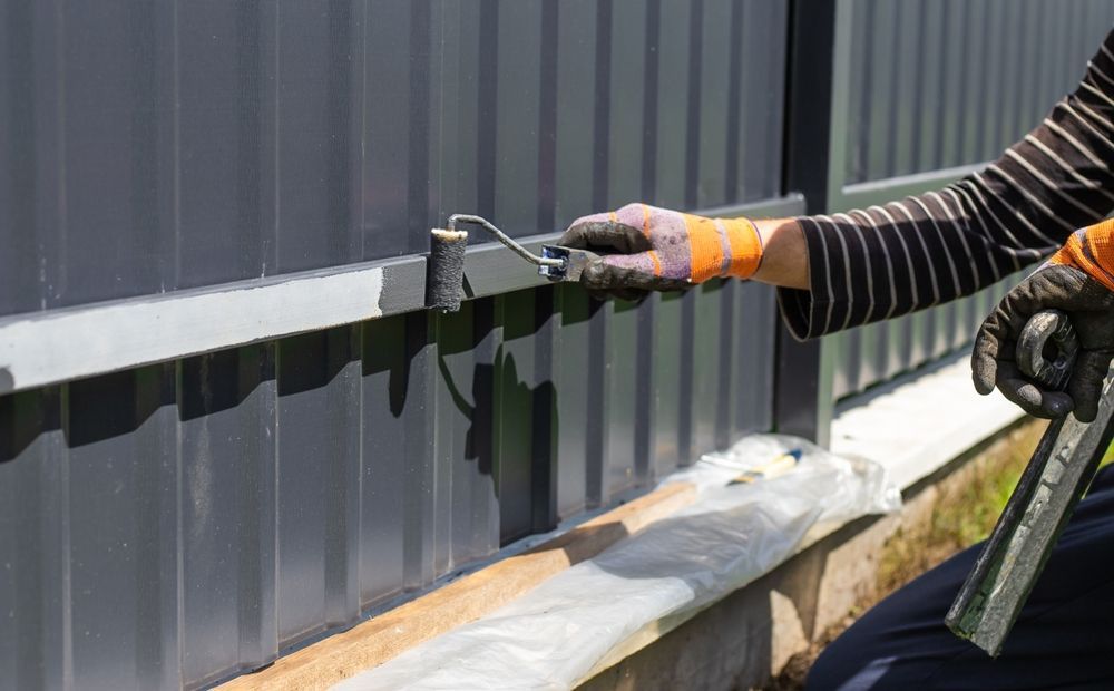 Person painting a gray metal fence with a roller — TMP Painting Services in Beaconsfield, QLD