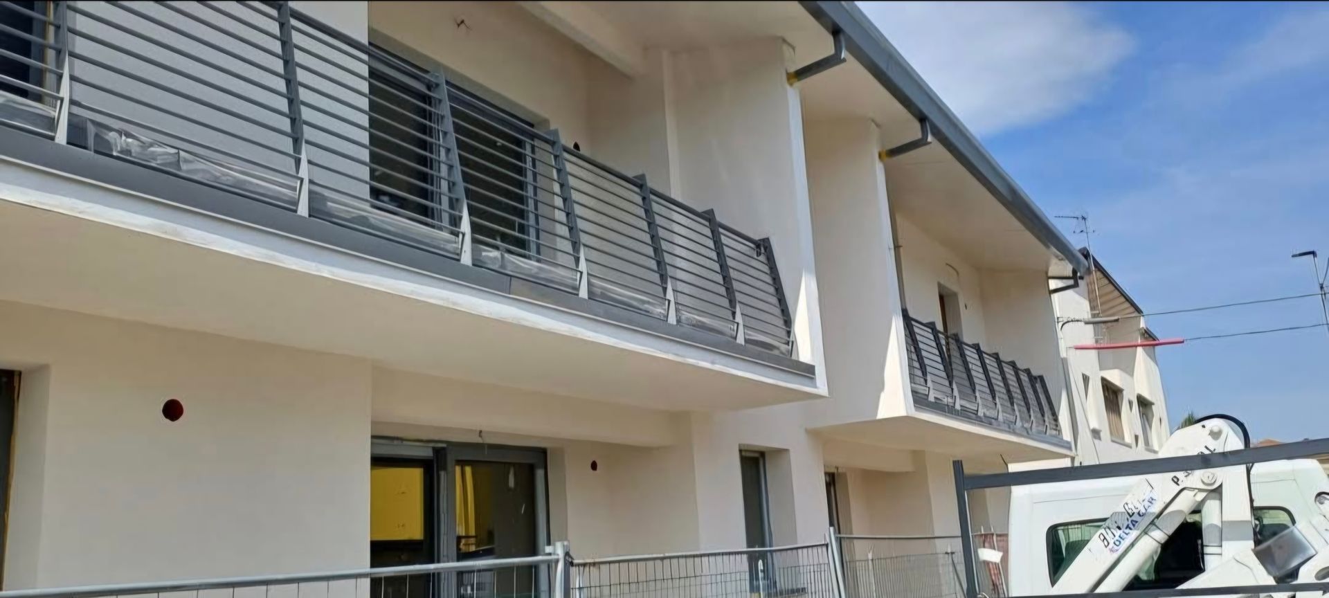 Edificio con balconi e ringhiere metalliche, sotto un cielo azzurro.