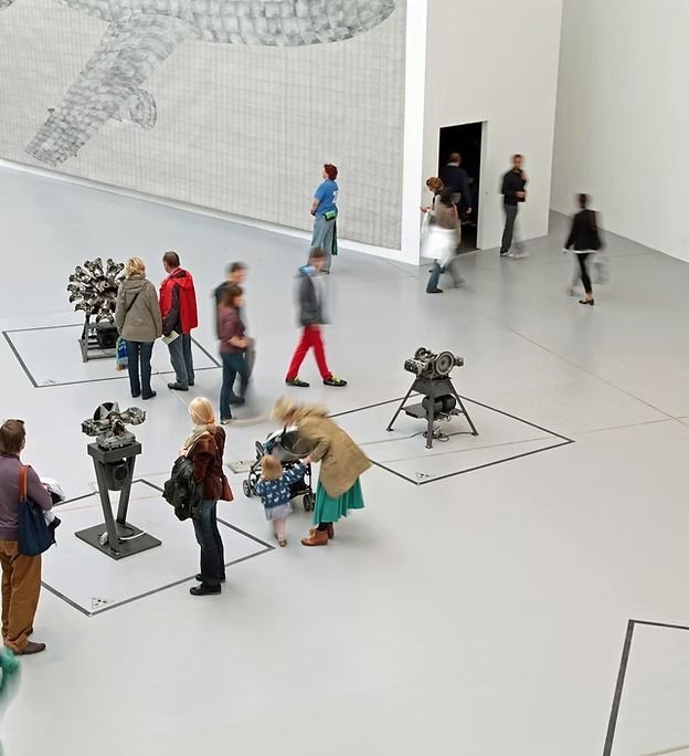 People viewing engine exhibits in a bright museum gallery with a large mural.