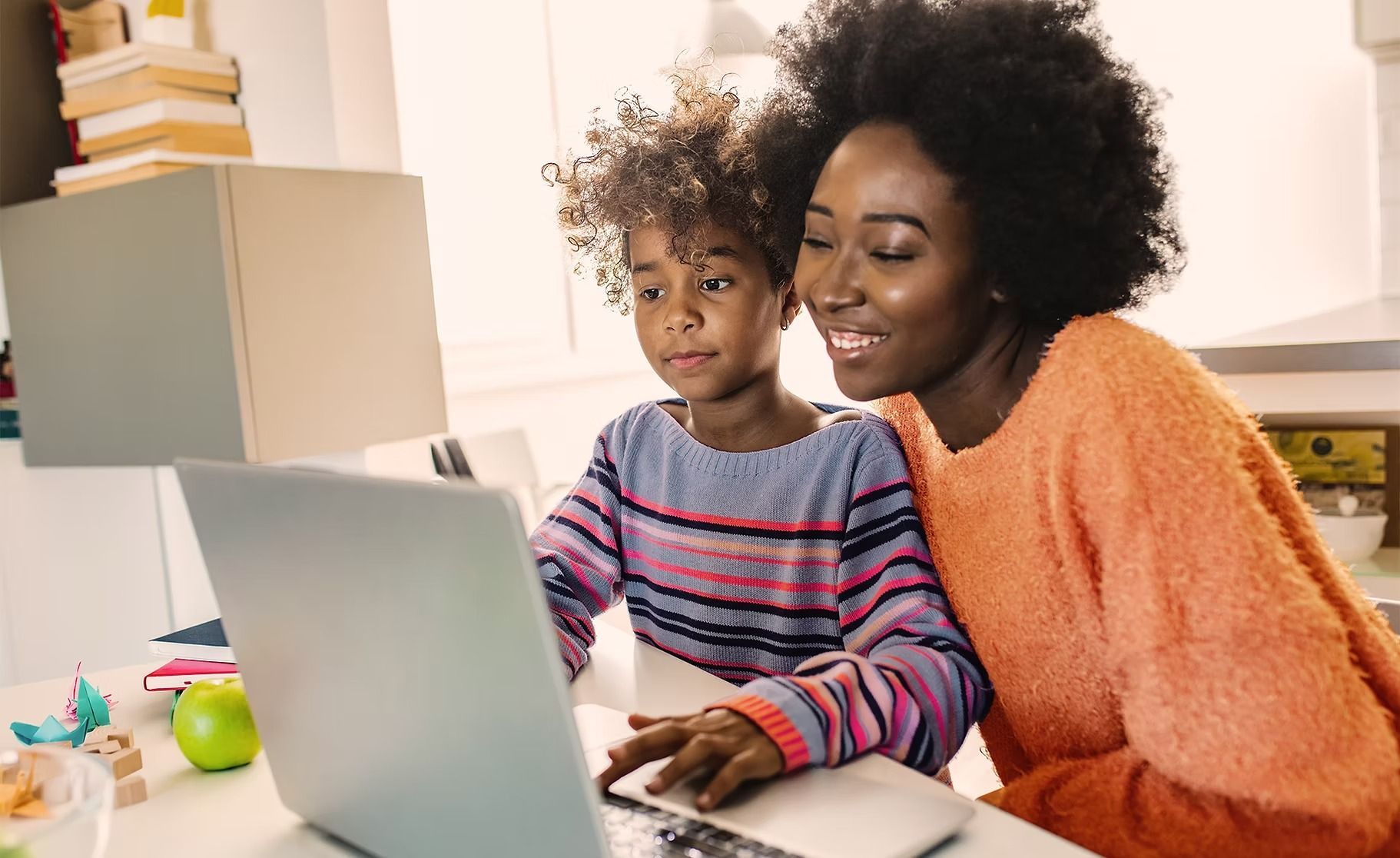 Woman and child smiling, looking at laptop screen. They are indoors.
