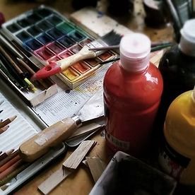 Art supplies on a table: paint palette, brushes, and bottles of red and yellow paint.