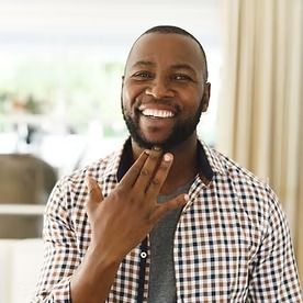 Man smiling, signing with hand; wearing plaid shirt.