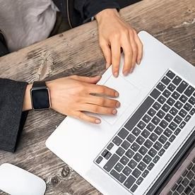Person using a laptop on a wooden desk. One hand on touchpad, the other near keyboard.
